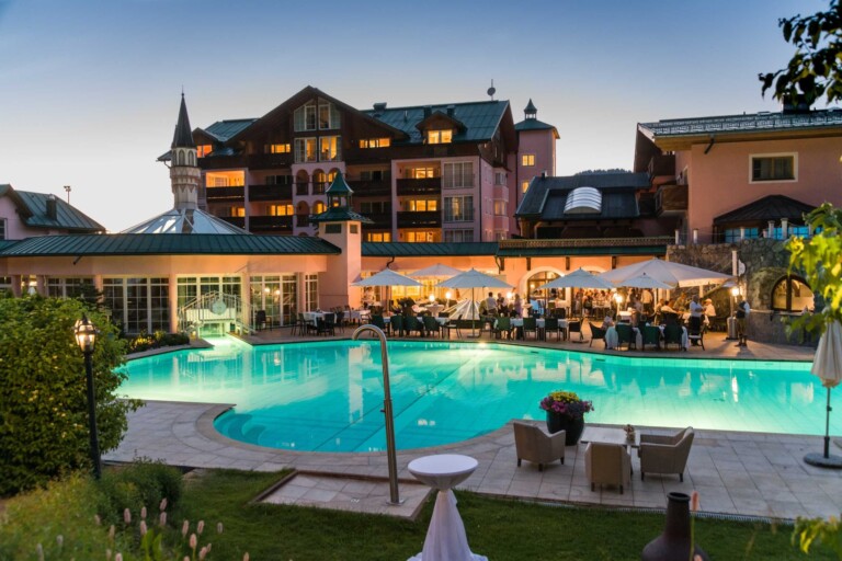 Beleuchteter Außenpool des Hotels ...liebes Rot-Flüh im Tannheimer Tal mit Terrasse und Blick auf das Hotel in der Abenddämmerung.