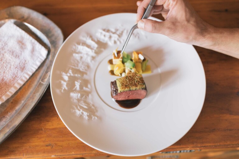 Koch verfeinert ein Fleischgericht mit Garnitur im Restaurant des Gourmethotels ...liebes Rot-Flüh in Tirol.
