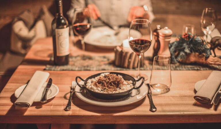 Rustikaler Tisch mit Fleischgericht und Rotwein im Erlebnisrestaurant des Hotels ...liebes Rot-Flüh in Tirol.