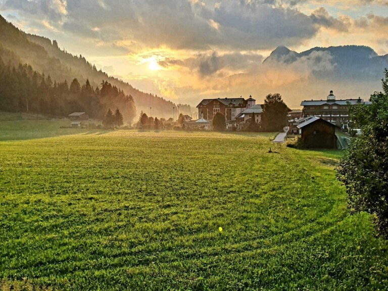 Sonnenaufgang im Tannheimer Tal mit Blick auf eine grüne Wiese und das Hotel ...liebes Rot-Flüh.