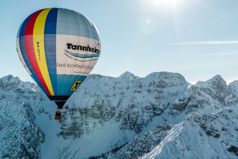 Heißluftballon von Sonne angestrahlt in einer winterlichen Berglandschaft im Tannheimer Tal.