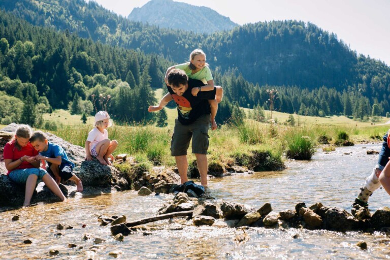 Familie am Bach beim Spielen während Familienurlaub im Tannheimer Tal.