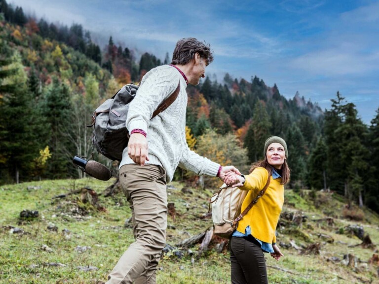 Paar hält Händchen auf einer Wanderung mit Wäldern im Hintergrund im Tannheimer Tal.