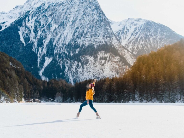 Frau auf einem zugefrorenen See mit Bergen im Hintergrund im Tannheimer Tal.