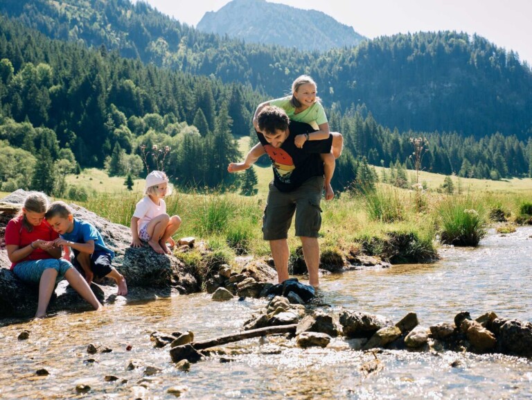Familie spielt am Bach umgeben von Wiesen und Bergwäldern im Tannheimer Tal.