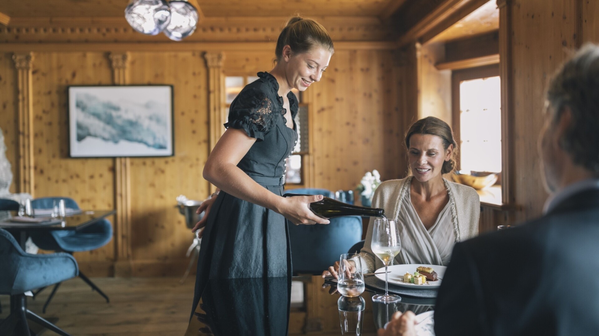 Servicemitarbeiterin serviert Gästen Wein im Gourmetrestaurant ...liebes Rot-Flüh.
